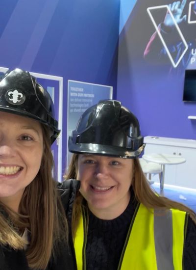 Two women wearing hard hats standing in a half built tradeshow booth