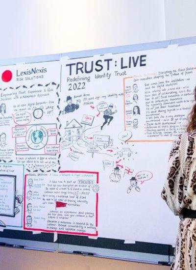A person drawing or writing on a white board that has Trust Live written on it