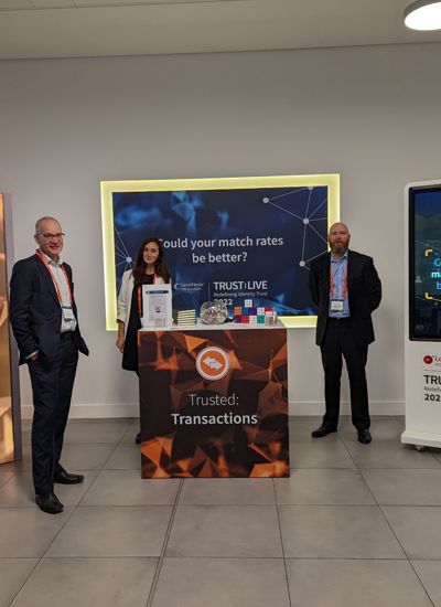 Three people standing next to a tradeshow booth called Trusted Transactions