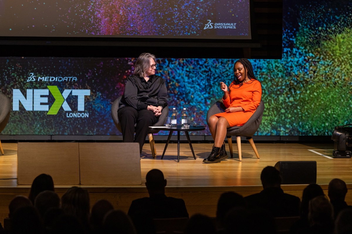 Two seated women on a stage talking in front of Medidata NEXT London signage