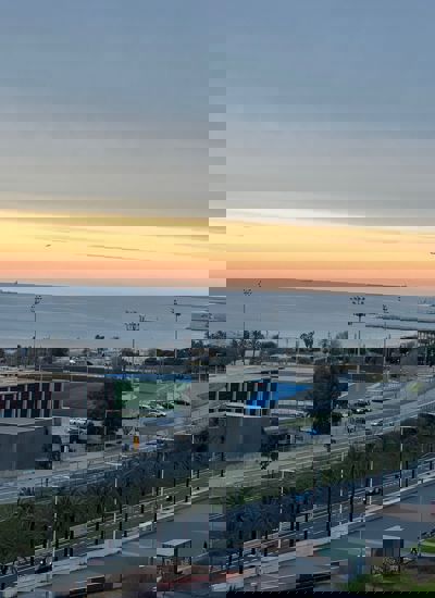 A view across a road and some playing fields to the sea and sun