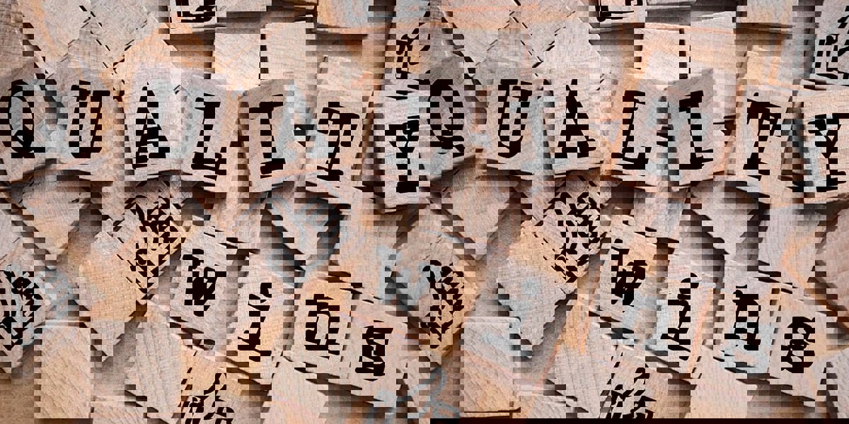 Wooden letters arranged to spell 'Quality Wins' surrounded by thumbs up