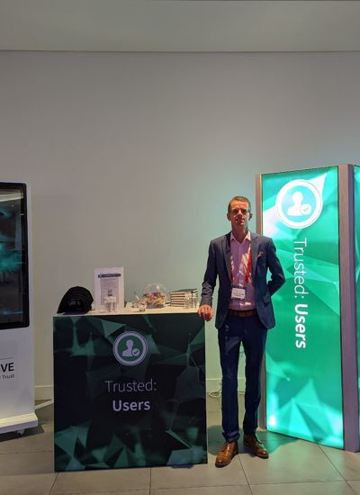 A man standing next to a tradeshow display called Trusted Users