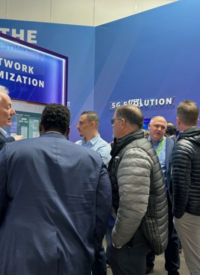 A group of men listening to a white haired man talking in a VIAVI tradeshow booth