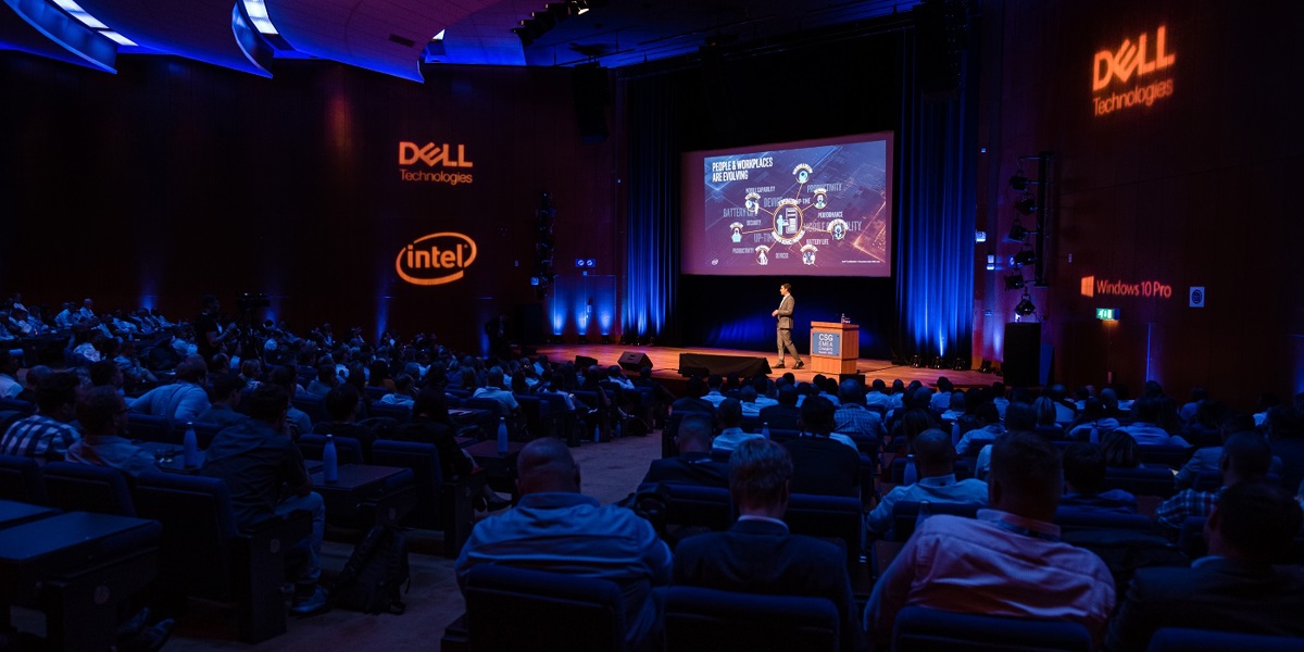A room full of seated people watching a presentation given by a person on a stage with Dell and Intel signage