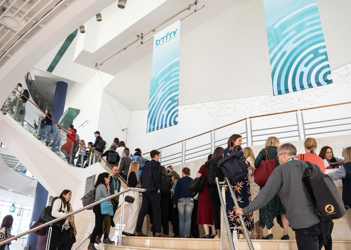 People on a staircase in a modern building with two large blue banners hanging from the ceiling