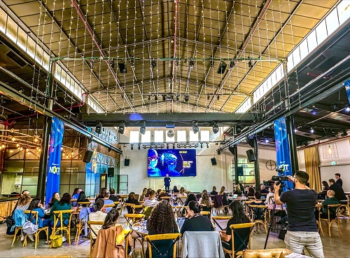 A large room with seated people a stage and a photographer