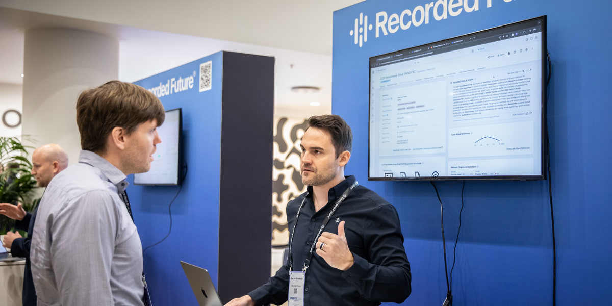 Two people talking at Recorded Future booth with screen showing cybersecurity info