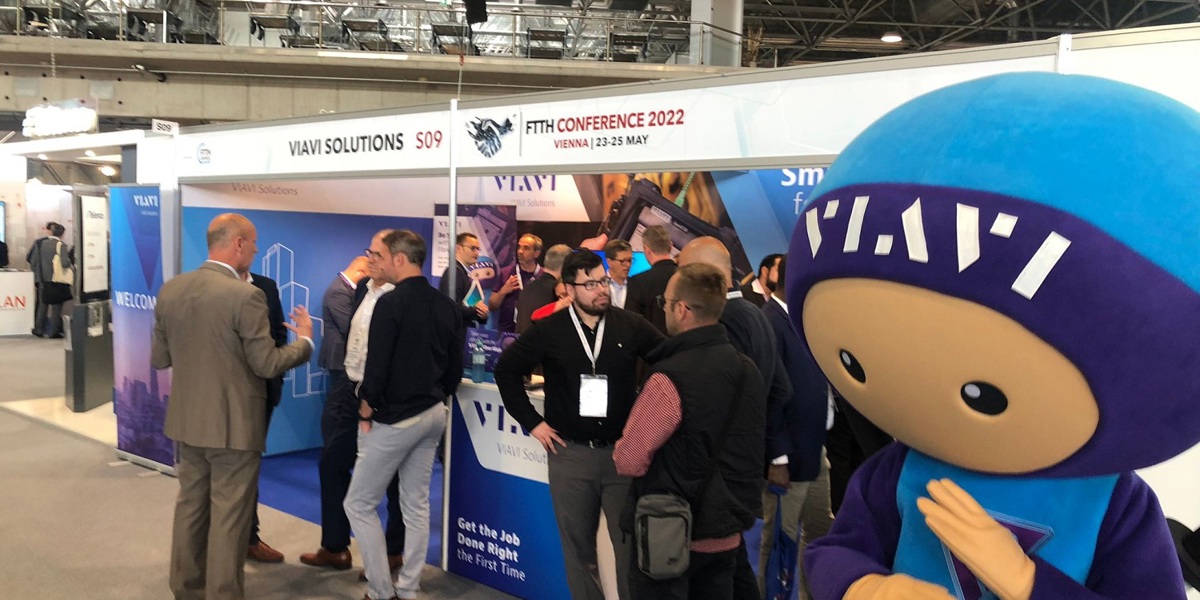 Attendees engaging at the VIAVI booth with a blue life sized mascot during the conference.