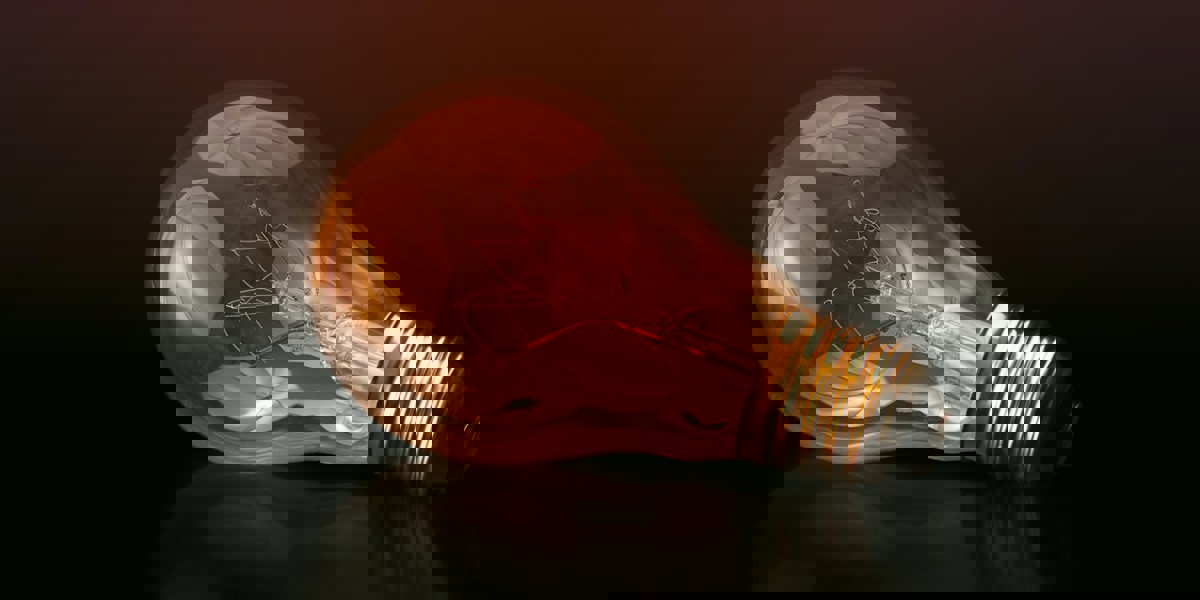 Glowing light bulb fallen on its side against a dark background representing disruption