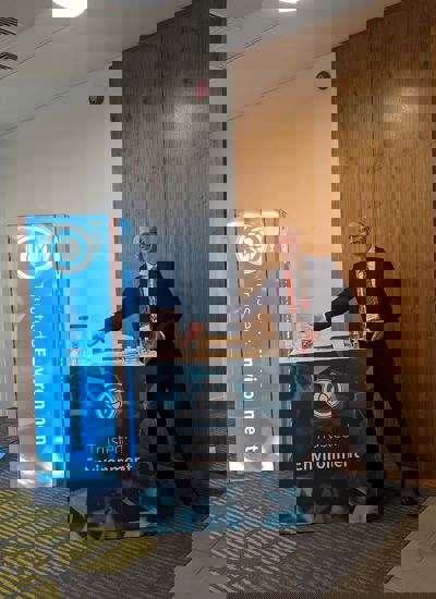 A man standing next to a tradeshow display called Trusted Environment