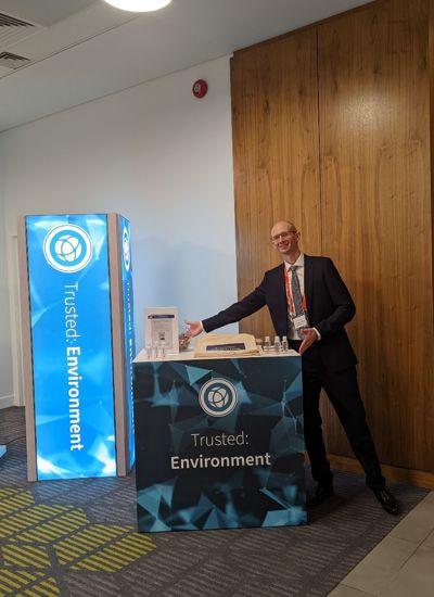 A man standing next to a tradeshow display called Trusted Environment