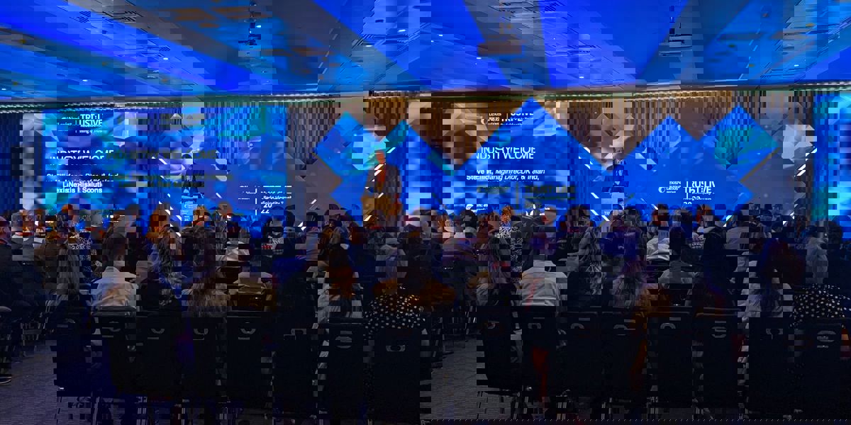 A room full of seated people watching a presentation given by a person on a stage