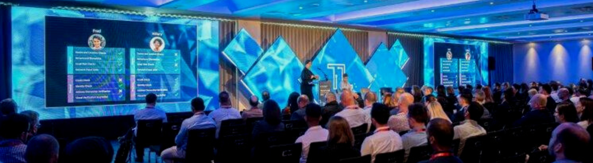 Event venue with a large presentation screen and audience seating in classroom layout.