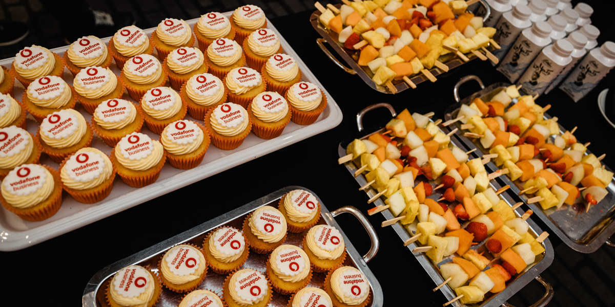 Table of food, including branded cupcakes and fruit skewers