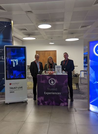 Three people standing next to a tradeshow booth called Trusted Experiences