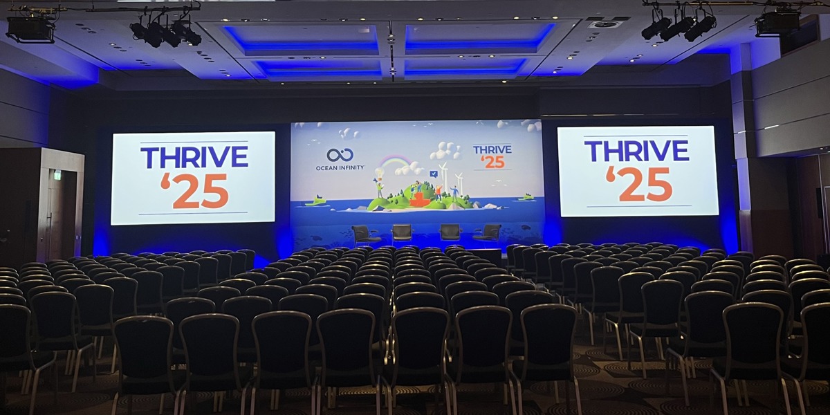 Stage setup for Thrive '25 with rows of chairs and three screens displaying event branding