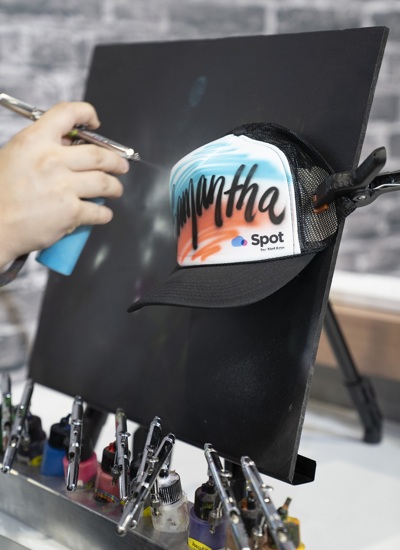 A person using an airbrush to decorate a baseball cap